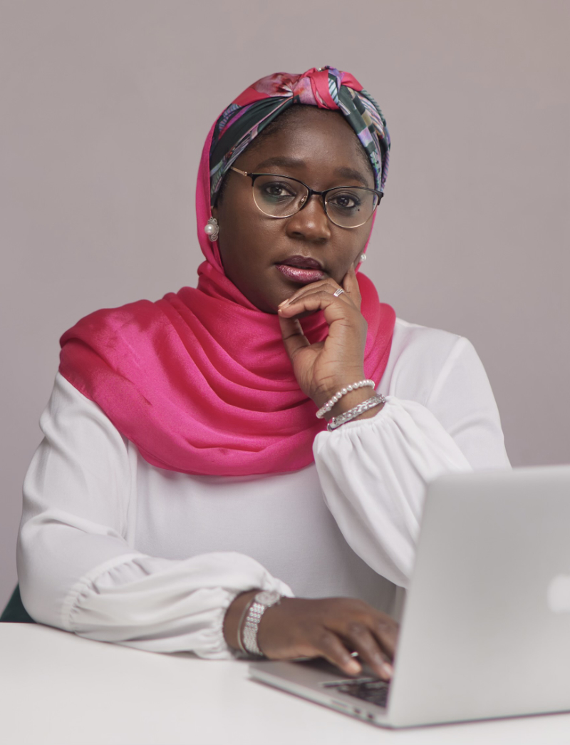 Portrait of Aisha A.U. Gumel sitting at a desk working on her laptop
